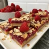 Hausgemachte fruchtige Himbeer-Mandel-Riegel mit frischen Himbeeren und Mandeln auf einem Holzbrett
