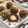 Nahaufnahme von Schoko-Nuss Energy Balls mit cremiger Füllung – gesunde Energiebällchen aus Datteln, Nüssen und Kakaopulver mit Nussmusfüllung auf Holzbrett