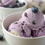 Cremiges Blaubeereis in einer Schale, garniert mit frischen Blaubeeren und Minze