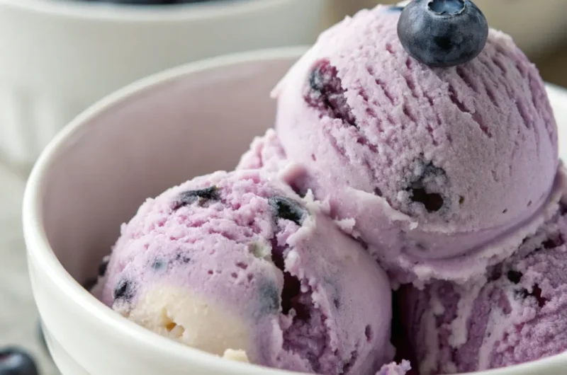 Cremiges Blaubeereis in einer Schale, garniert mit frischen Blaubeeren und Minze